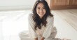 © MD Media - Happy Smiling Asian woman sitting cross legged on the floor and smiling. Wellness and fitness concept