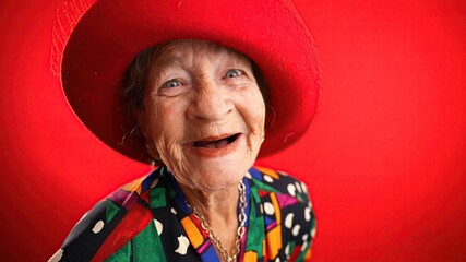 Poster - Smiling distorted fisheye portrait caricature of funny elderly woman smiling with red hat and no teeth isolated on red background.