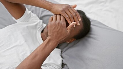 Wall Mural - Shocked african american woman covering eyes and mouth with hands in surprise, lying on bed in a bedroom, expertly hiding emotions