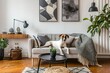 © Azar - Stylish and scandinavian living room interior of modern apartment with gray sofa, design wooden commode, black table, lamp, abstrac paintings on the wall. Beautiful dog lying on the couch. Home decor.