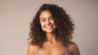 © Studio Nova - Woman with voluminous curly hair and a beaming smile, wearing a tank top and posing against a warm beige background.