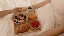 An intimate closeup capturing an unknown couple savoring a delightful breakfast in bed. A man serves muesli, juice, and berries to his girlfriend on a tray
