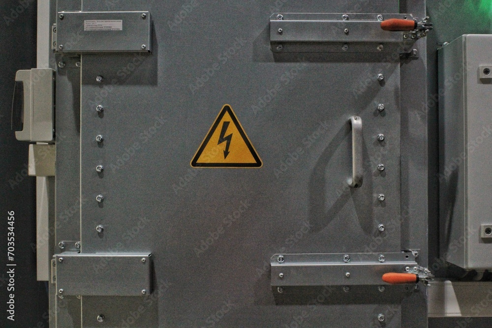 High voltage sign on the wall of a gate power plant. Industrial safety warning sign. Electricity switching station. Metal gray doors of  transformer box electrical substation