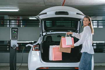 Young woman travel with EV electric car to shopping center parking lot charging in downtown city showing urban sustainability lifestyle by green clean rechargeable energy of electric vehicle innards