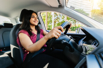 Young adult happy indian woman driving a car in the city. Rental car service concept