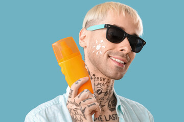 Wall Mural - Tattooed man with sunscreen cream on light blue background