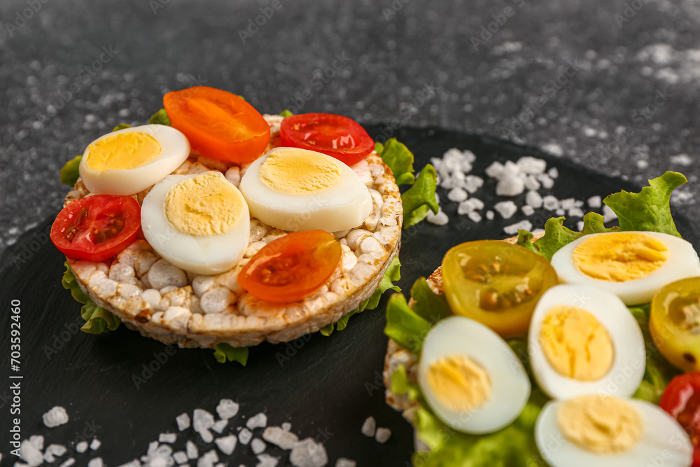 Rice crackers with quail eggs, tomatoes and lettuce on dark grunge background, closeup