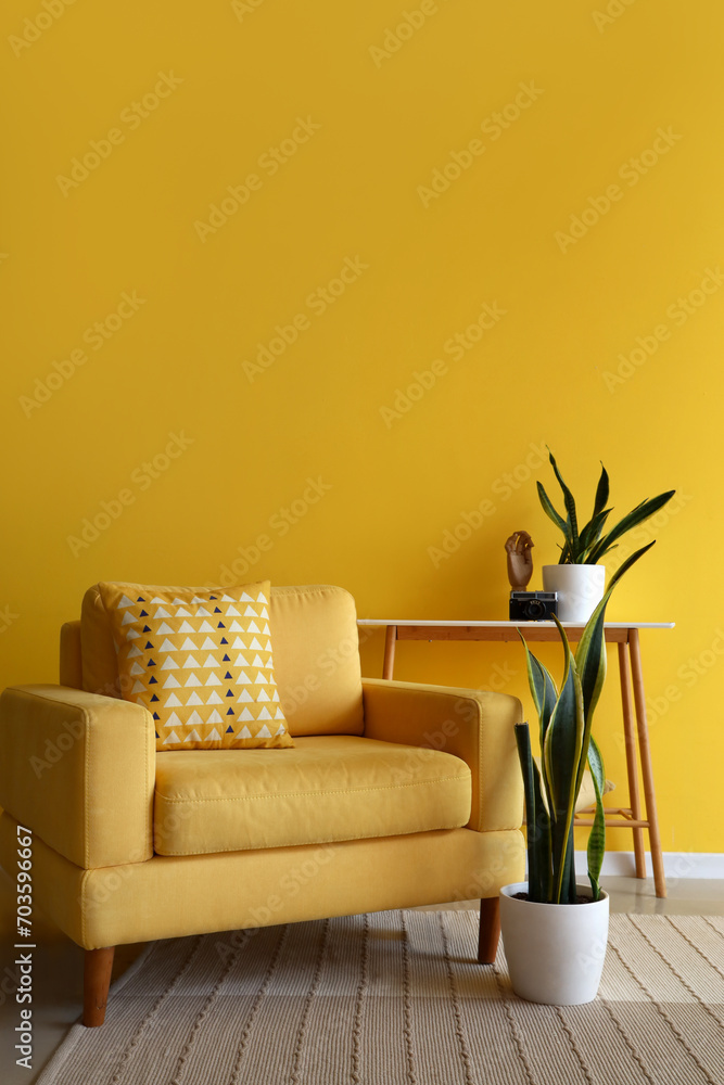 Comfortable armchair, console table and houseplants near yellow wall