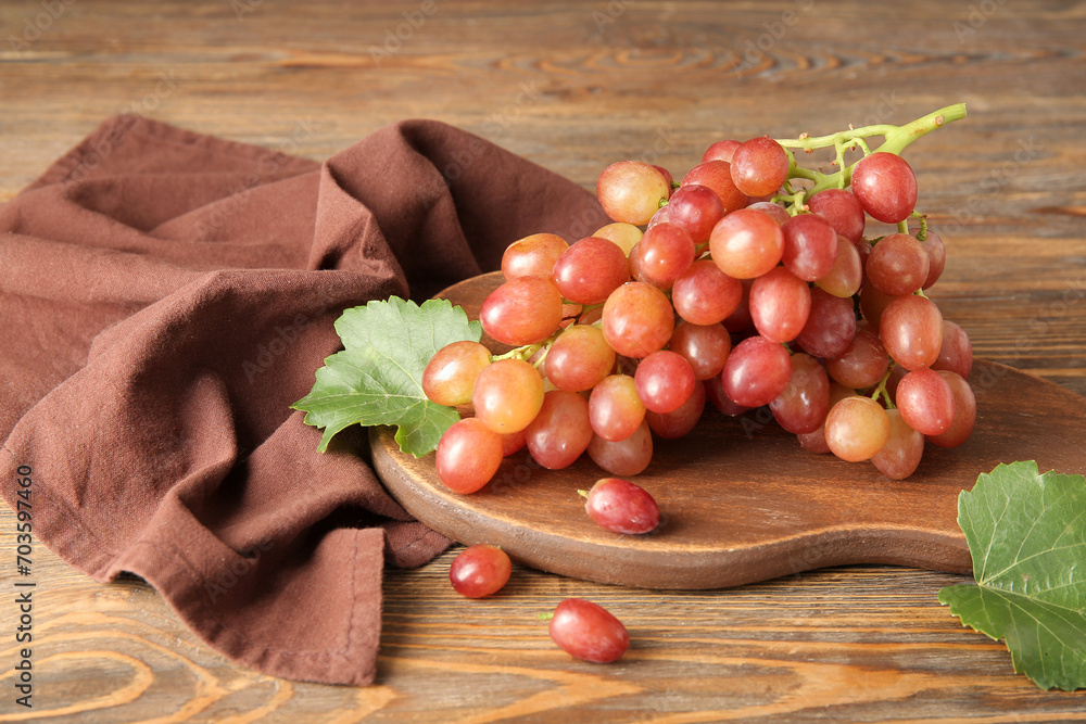 Board with tasty ripe grapes on wooden background