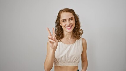 Poster - Cheerful young woman points confidently upwards, flaunting number two gesture with fingers against isolated white background. attractive female smiling happily, showcasing positive expression