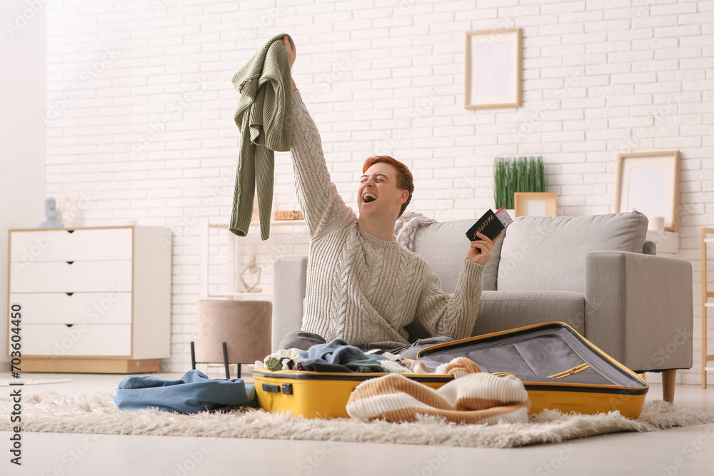 Happy young man with passport packing suitcase at home