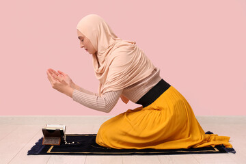 Wall Mural - Young Muslim woman praying on pink background