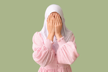 Wall Mural - Young Muslim woman praying on green background