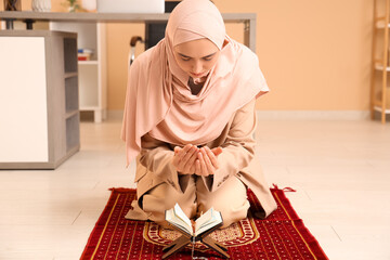 Wall Mural - Young Muslim woman with Koran praying in office