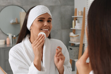 Wall Mural - Young woman cleaning her face with cotton pad near mirror in bathroom