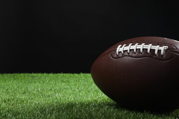 Wall Mural - Leather American football ball on green grass against black background, closeup. Space for text