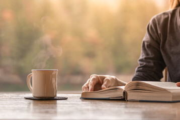 Wall Mural - Person reading book and enjoying a cup of coffee early morning 