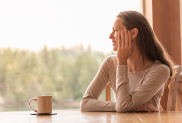 Wall Mural - Young woman relaxing looking out window early morning  at the beautiful nature view, enjoying coffee and quiet time. 