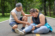 © kudosstudio - Overweight young woman with knee pain sitting on the running track at local park with both hands grabbing on her trouble knee while a middle age man kneeling beside her helping with concern