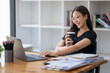 © Wasana - Freelance Asian businessperson, businesswoman sitting and enjoying hot coffee, pay attention on the laptop screen while relaxing.
