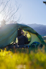 Sticker - child sits in a tent and drinks water from a bottle. boy in a sleeping bag. portrait of a child in a tent.  camping and trekking with children.