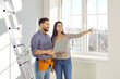 © Studio Romantic - Young married couple is planning an apartment renovation and design project standing in empty room after moving day. Smiling happy man and woman with laptop discussing repair of their new home.