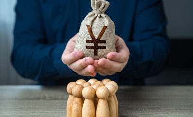 Wall Mural - A man is holding a chinese yuan or japanese yen money bag over a group of people figurines. Political lobbying. Generation of funds. Organization of the community budget. Payment for labor