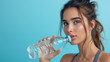 © ND STOCK - Fit and Refreshed: Woman taking a sip from a water bottle in fitness clothing on a blue background with space for text. Copy space. Active lifestyle and Wellness concept