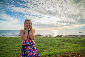 A young beautiful woman traveler in a colorful summer dress is enjoying herself on the coast