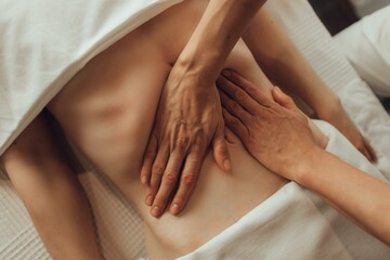 Wall Mural - Hands of female chiropractor massaging belly of young woman lying on massage table on white background. Visceral massage. Concept of physical therapy treatment, neck pressure point.