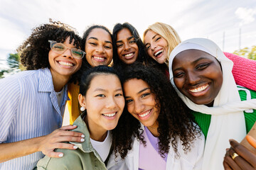 Wall Mural - Group portrait of happy diverse women standing together outdoors. Millennial female friends from different cultures smiling at camera. Friendship and youth community concept.