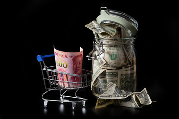 100 Chinese yuan bill in shopping cart and glass jar with 1 US dollar bills