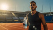 Latino male sprinter athlete on a track holding in his hand and drinking cold isotonic sports water drink, sweaty after exercises