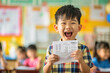 Joyful young boy smiling and holding up his excellent report card in a vibrant school classroom.