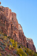 The steep mountain cliffs of zion national park. Blue sky is overhead, and barely seen in the distance is the moon