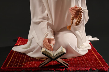 Wall Mural - Young Muslim woman with Koran and beads praying on black background