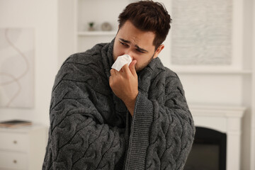 Sticker - Sick man wrapped in blanket with tissue blowing nose at home. Cold symptoms