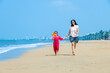 © GAJENDRRA BHATI  - Happy Indian mother and daughter running on tropical beach and enjoying summer vacation. daughter playing with paper windmill on sea side.