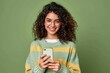 Young adult smiling happy pretty latin woman holding mobile phone looking at camera, doing ecommerce shopping on smartphone, using trendy dating apps on cellphone isolated on green, Generative AI 