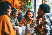 A Diverse Group Of Young Adults Enjoying A Warm Conversation Over Coffee In A Cozy Cafe Setting.