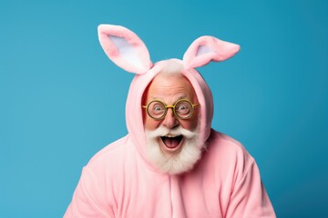 An elderly smiling pensioner man in a pink rabbit suit on a blue background. concept of a happy Easter.