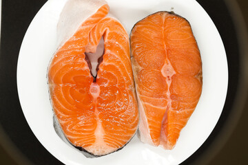 Two juicy salmon steaks on a white plate on a black background