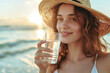 © Keitma - Hydration concept image with young beautiful girl drinking a glass of water on the beach on hot sunny summer heatwave day
