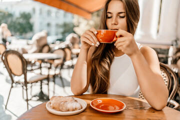Portrait of happy woman sitting in a cafe outdoor drinking coffee. Woman while relaxing in cafe at table on street, dressed in a white T-shirt and jeans