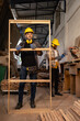 © Wanwajee - Young White man standing with window work peice with blur American Affrican men carpenter labor, craftmen working in wood workshop together with seriously in furniture industry.