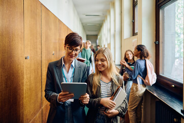 Happy high school teacher and her student using touchpad in hallway.