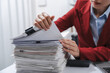 Close up hands of person in a red blazer organizing a substantial stack of various papers, likely sorting or reviewing documents for yearly tax purposes.