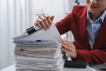 Close up hands of person in a red blazer organizing a substantial stack of various papers, likely sorting or reviewing documents for yearly tax purposes.