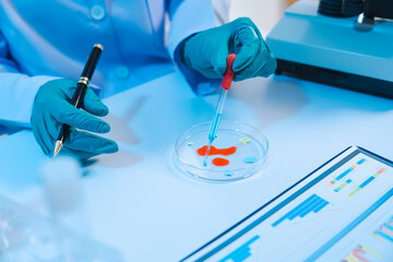 Sticker - Asian people scientist in lab coat and protective gloves working with test tubes with green and red liquids, with microscope and other test tubes in the background in laboratory.