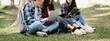 © Nuttapong punna - Three young college students is reading a book while relaxing sitting on grass in a campus park with her friends. Education concept